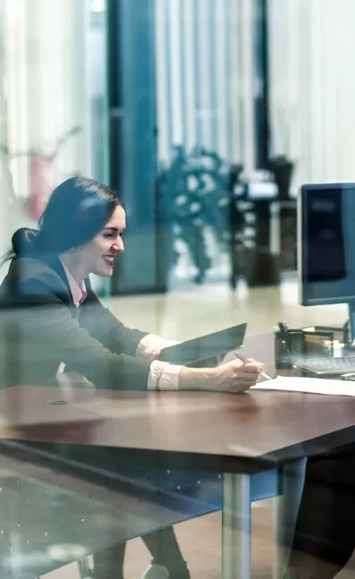 Smiling businesswoman working at desk with tablet and documents, reflecting efficiency and productivity in a modern office setting.