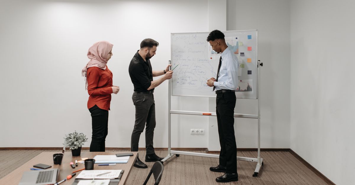 Three professionals discussing project ideas during an office meeting, illustrating teamwork and diversity.