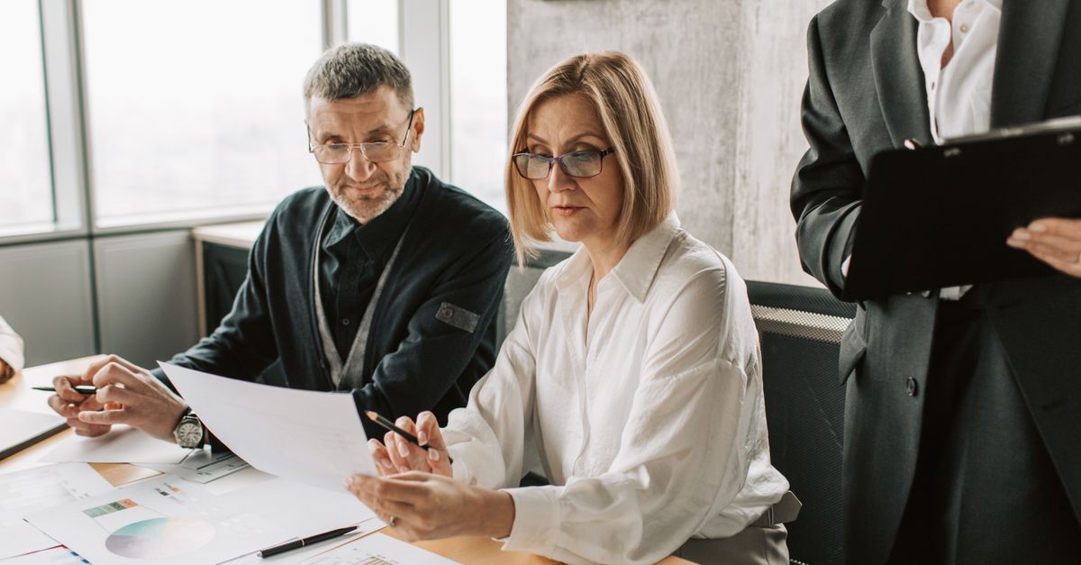 Business professionals engaged in a meeting, analyzing documents and charts in a modern office.