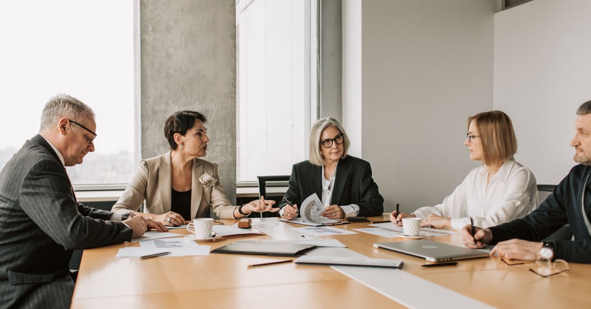 Five business professionals engaged in a meeting in a modern office setting, discussing documents and ideas.