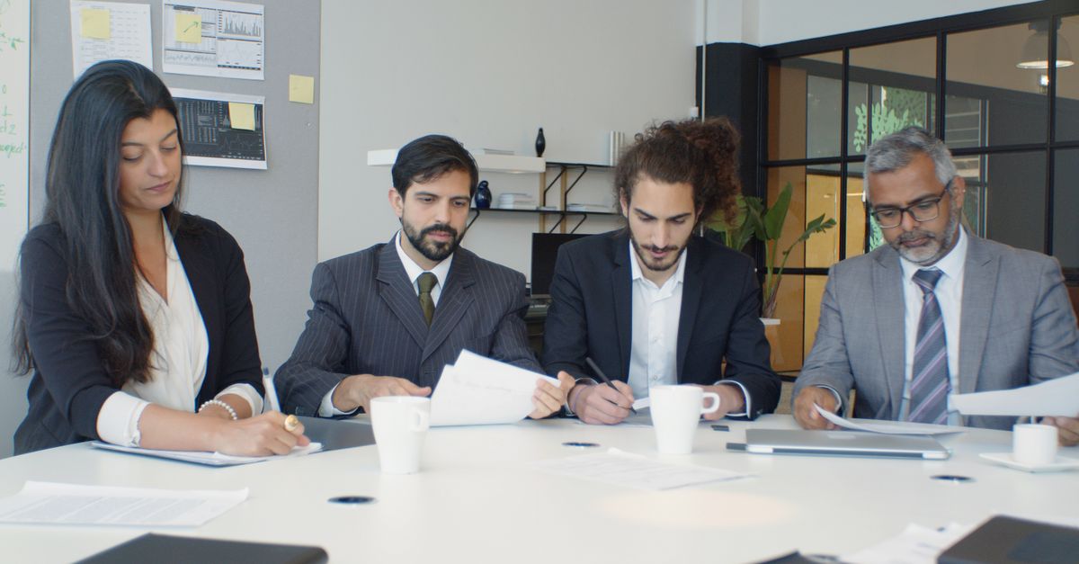Group of business professionals engaged in a team meeting around a desk in a modern office setting.