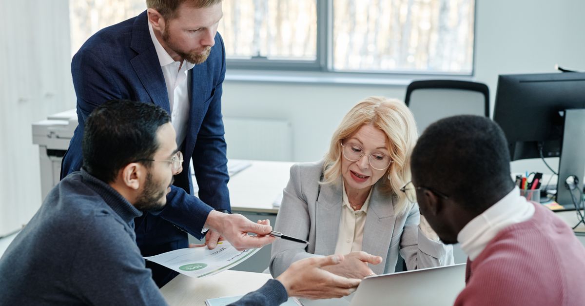 A diverse group of professionals engaged in a collaborative office meeting with laptops and documents.