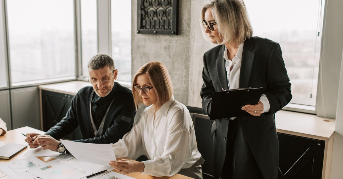 A group of business professionals discussing documents at a conference table in a modern office environment.