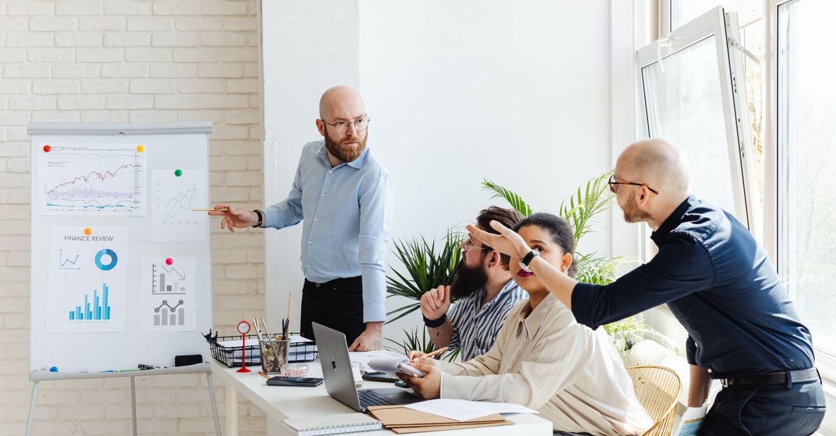 A group of professionals engaged in a business meeting, discussing financial graphs on a whiteboard.