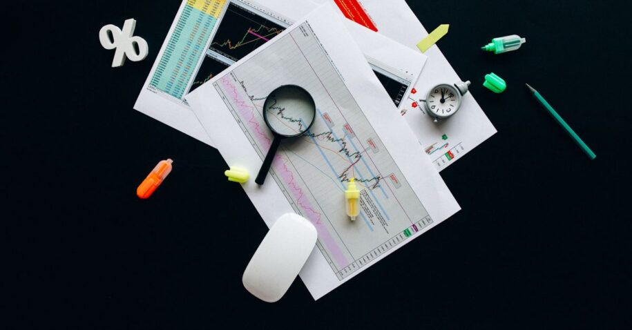 Overhead view of an office desk with financial documents, a magnifying glass, and stationery items, suggesting business analysis.