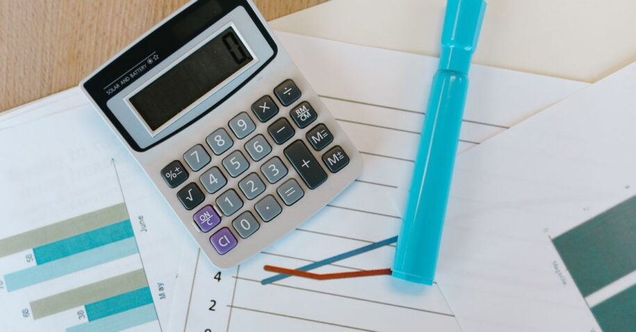 Top view of a calculator and charts on a wooden office desk with a blue marker.