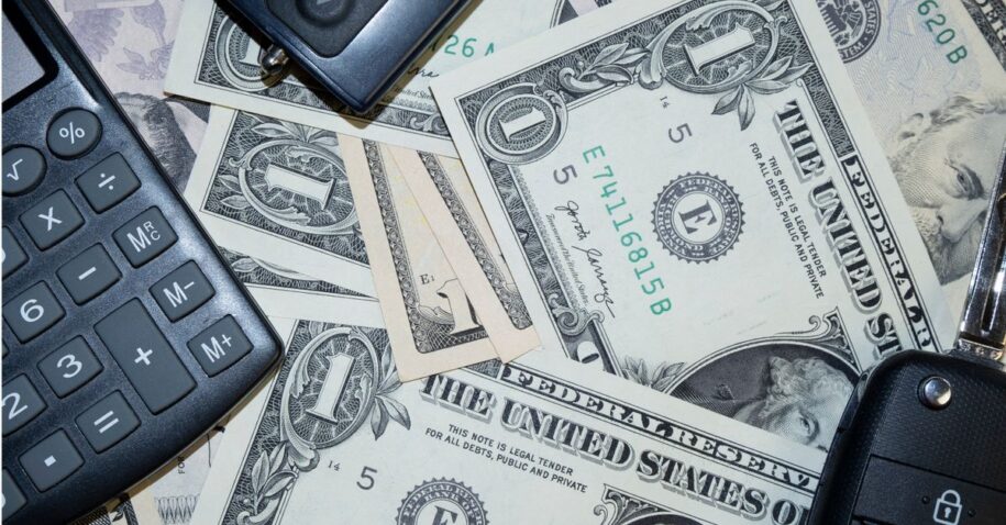 An arrangement of US dollar bills, car keys, and a calculator representing finance and investment concepts.