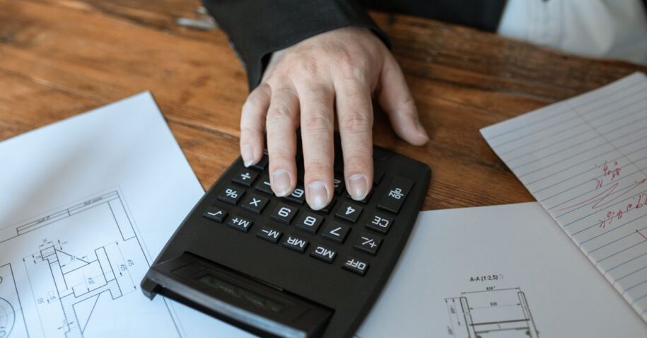Hand using calculator for architectural calculations on blueprints.