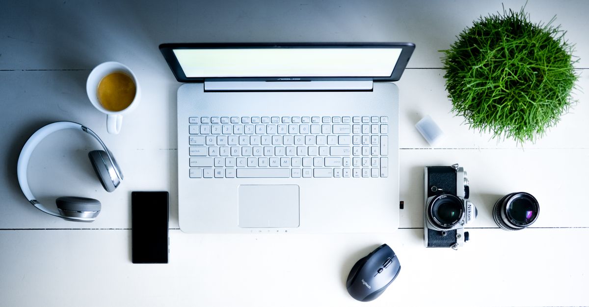 Overhead view of a desk with laptop, camera, lenses, and coffee in a minimalist setting.