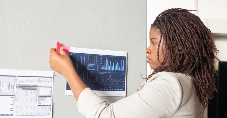 Focused businesswoman evaluating data analysis charts on office wall for strategic planning.