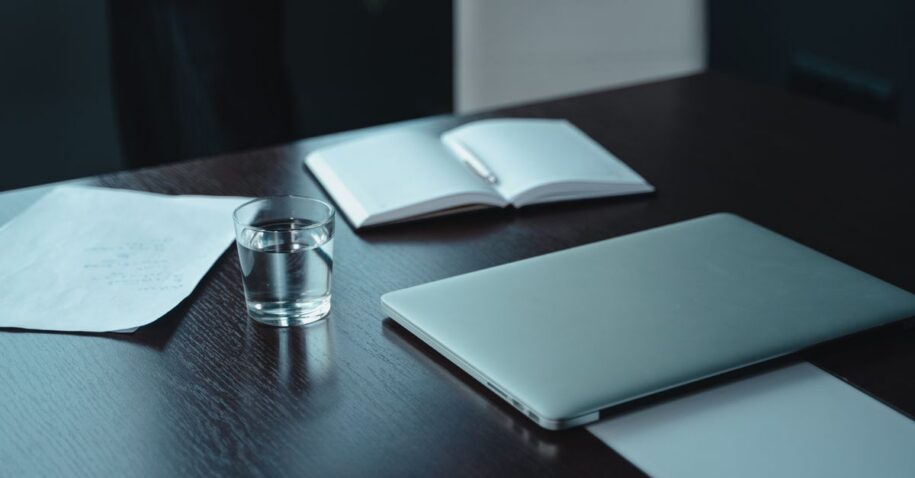 A modern workspace featuring a laptop, notebooks, and a glass of water on a wooden table.