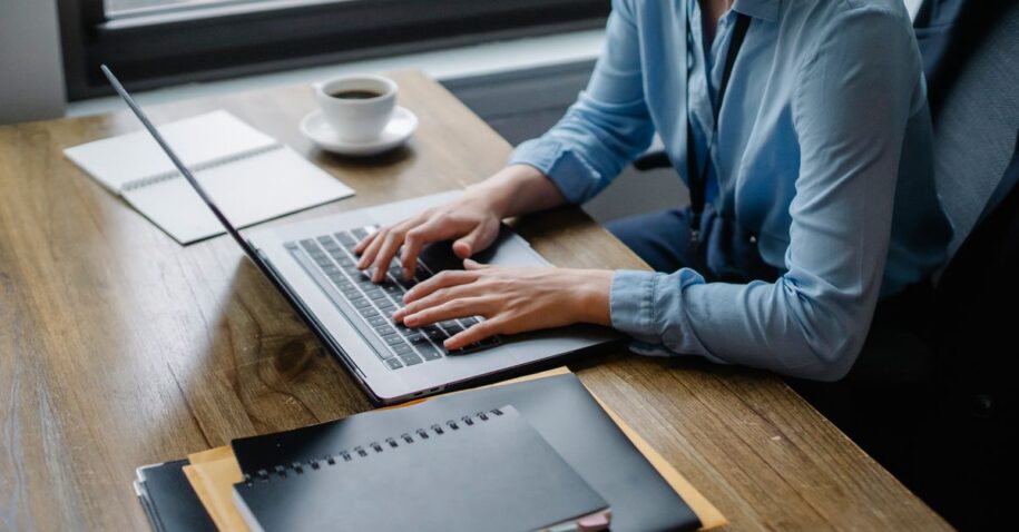 Office worker typing on laptop with coffee and notebooks on desk, capturing a focused work setting.