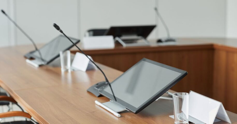 A modern conference room featuring sleek monitors and microphones on a wooden tabletop, perfect for meetings.
