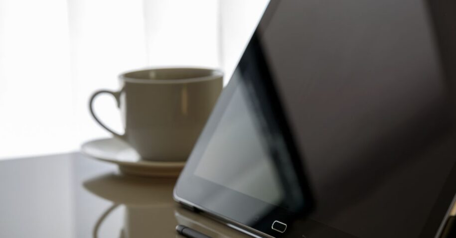 Modern tablet and coffee cup on a reflective desk, perfect for tech-related content.