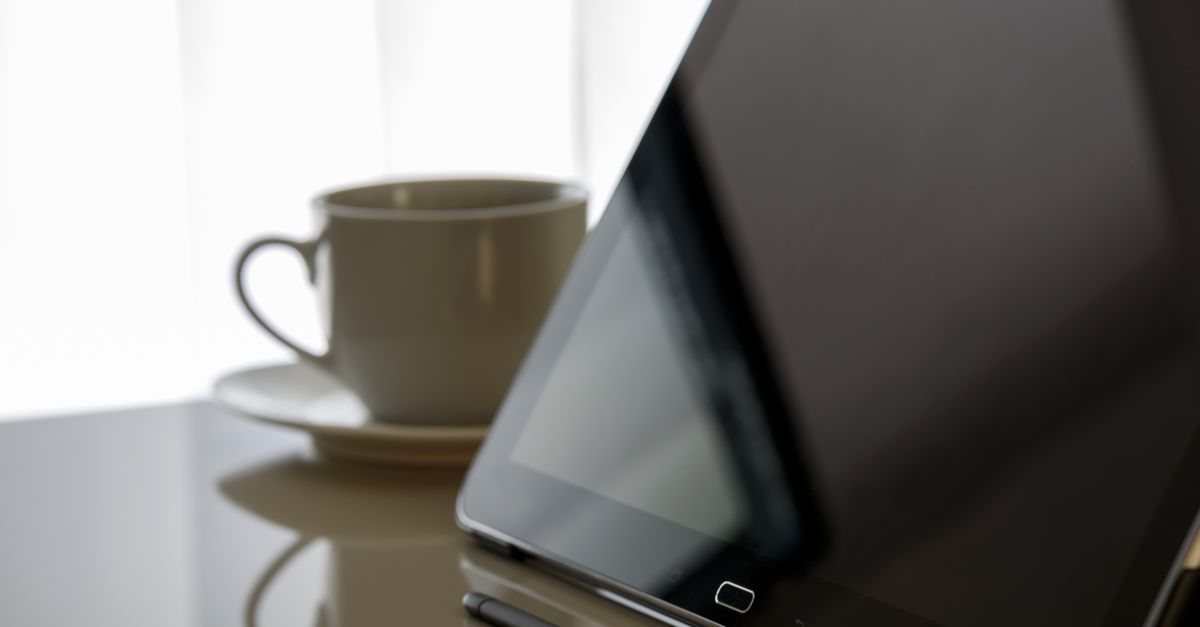 Modern tablet and coffee cup on a reflective desk, perfect for tech-related content.