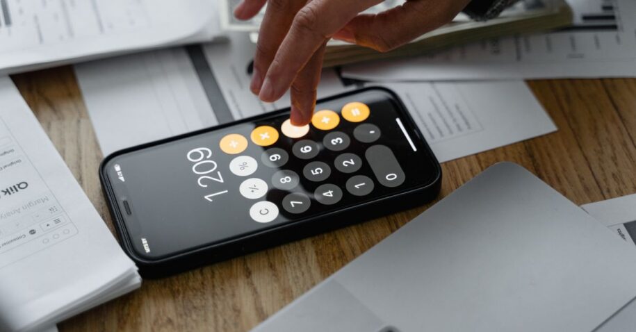 Close-up of a person using a smartphone calculator on a table with documents for financial calculations.