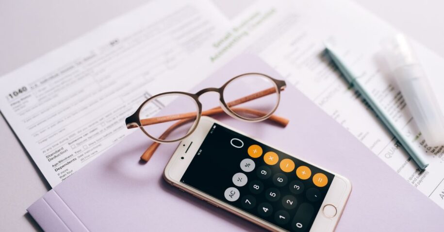 A smartphone calculator and glasses on tax documents, representing modern tax preparation.