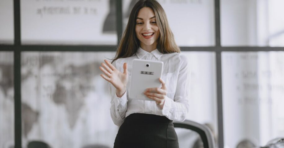A smiling brunette woman in a professional office setting using a digital tablet for work.