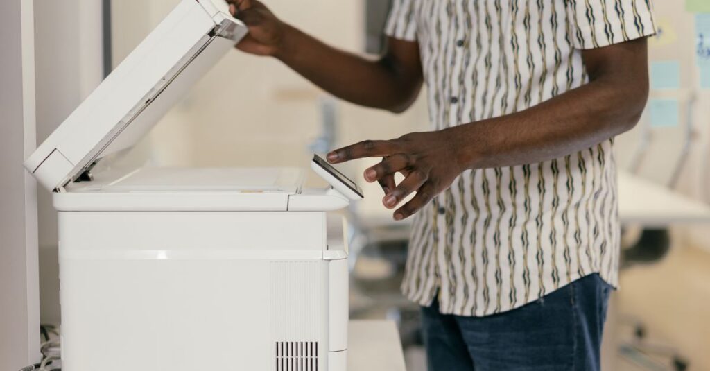 Person operating photocopier in modern office setting, engaging with technology.