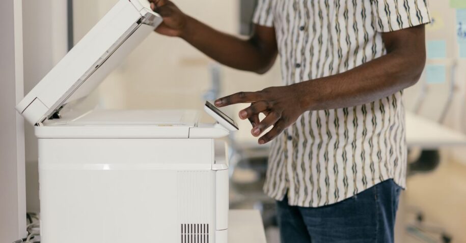 Person operating photocopier in modern office setting, engaging with technology.