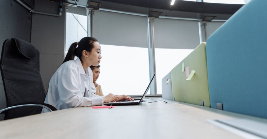 Two professionals working on laptops in a modern office setting with natural light