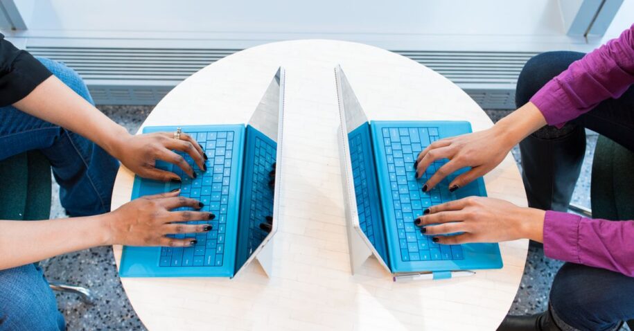 Two people working on blue laptops at a round table, focusing on teamwork and technology.