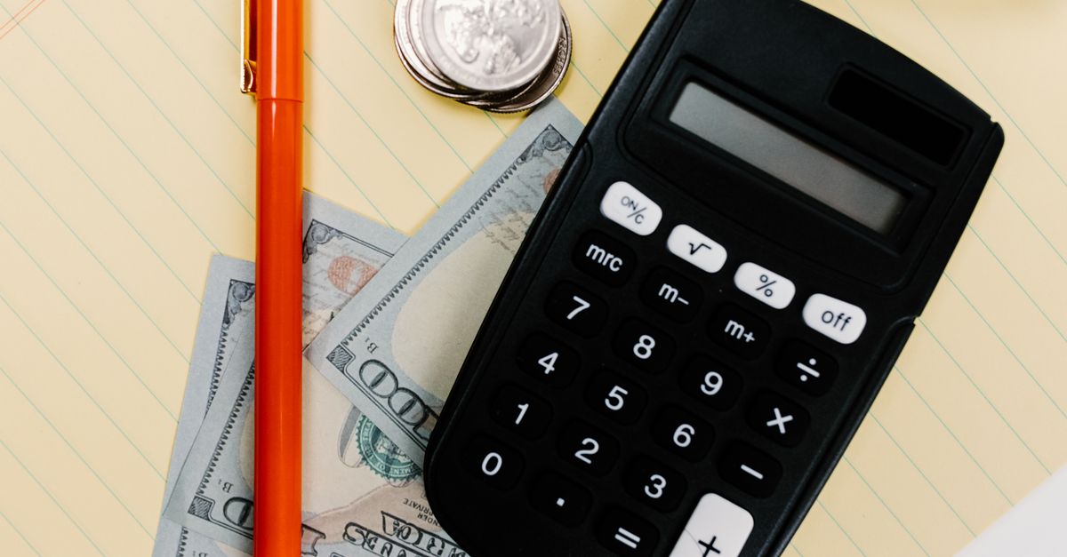 Close-up image of a calculator, pen, and currency on a yellow notepad, symbolizing finance.