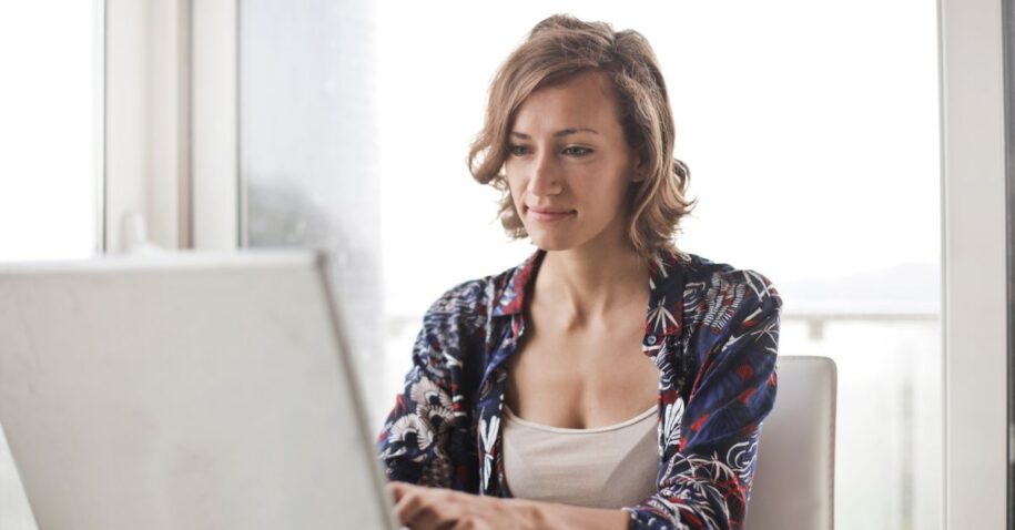 A woman typing on a laptop in a bright, modern home office setting.